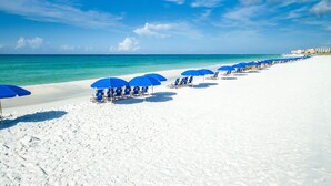 Ein Strand mit Reihen blauer Sonnenschirme und Liegestühle, ein klarer, blauer Himmel und ein ruhiges Meer.
