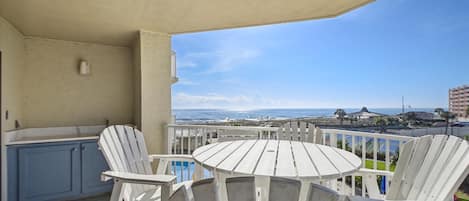 A balcony with a view of the ocean, white chairs, and a small table.