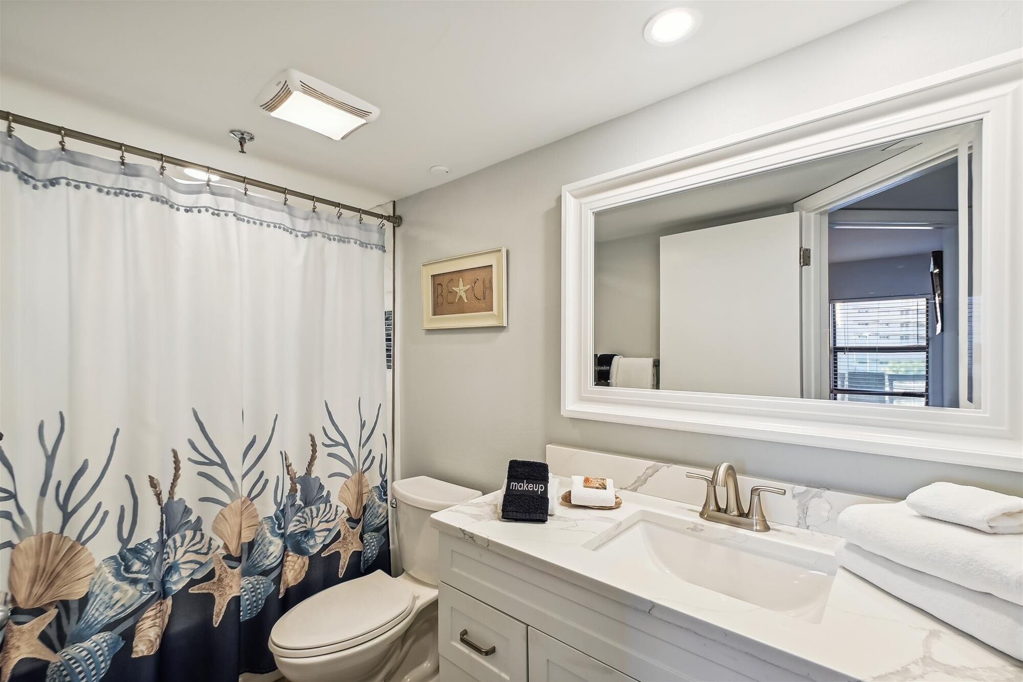 Un baño con inodoro, lavamanos y cortina de ducha con motivos marinos.