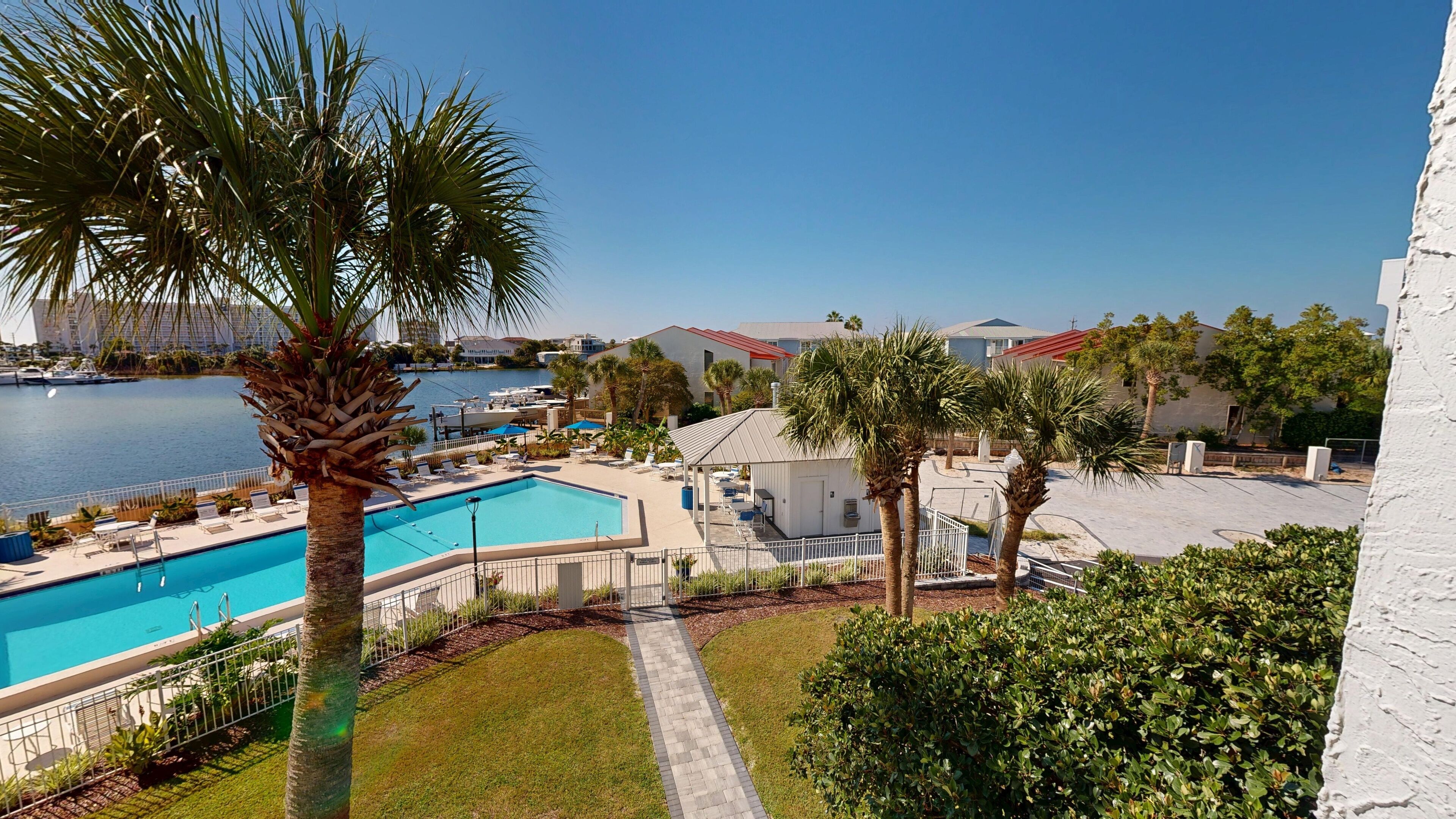 A swimming pool with lounge chairs, a covered seating area, and a view of the water and buildings in the background.