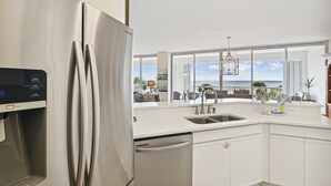 Una cocina moderna con un refrigerador de acero inoxidable, dispensador de agua y lavavajillas. Cuenta con un ventanal con vista al océano.