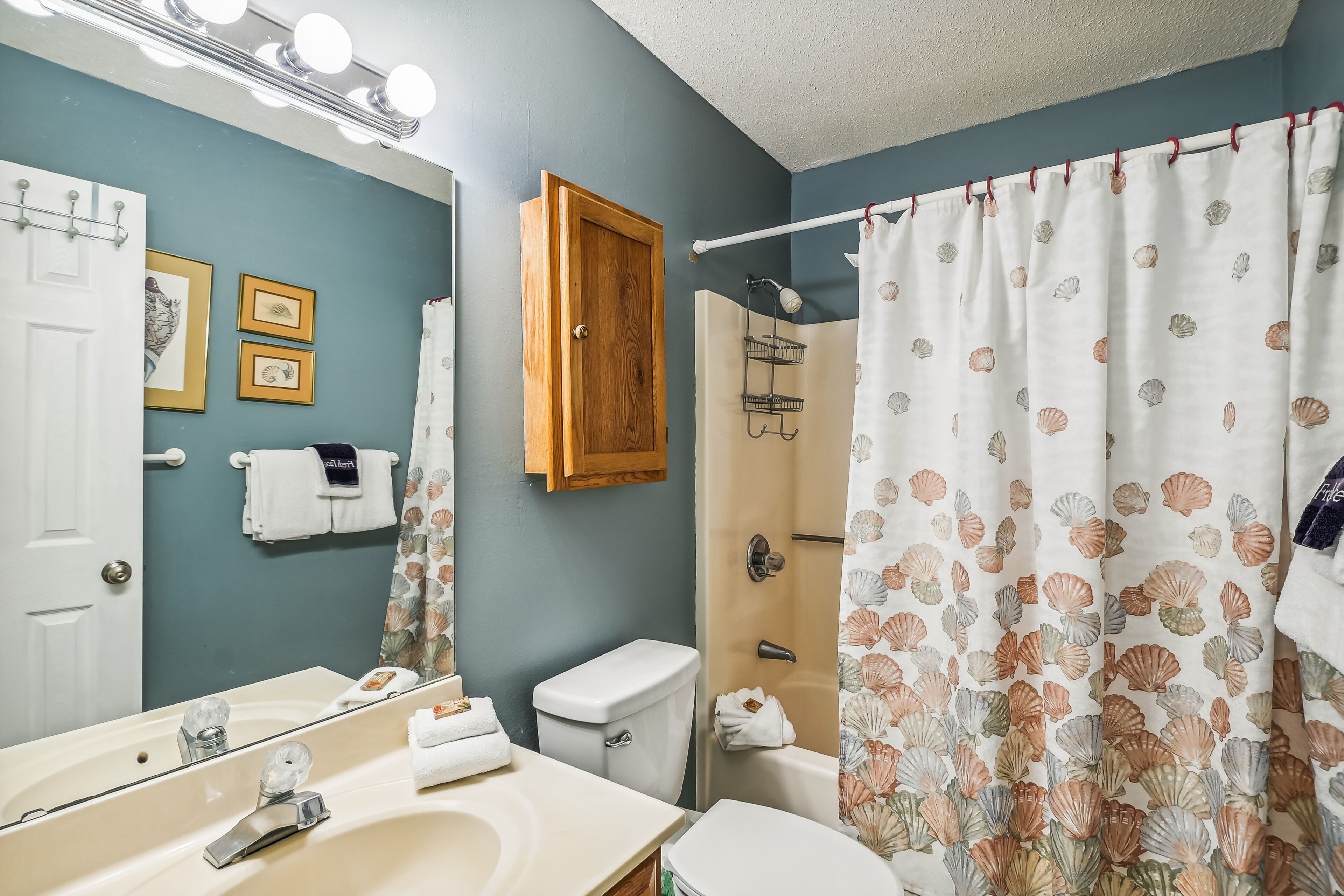 A bathroom with a sink, mirror, toilet, shower, and a wooden cabinet.