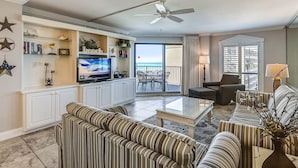 A spacious living room with striped sofas, a flat-screen TV, and a balcony with a view. - Inlet Reef 516 2 Bedroom Condo by RedAwning (Destin)