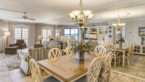 A spacious dining area with a large wooden table, white chairs, and a chandelier. - Inlet Reef 516 2 Bedroom Condo by RedAwning (Destin)