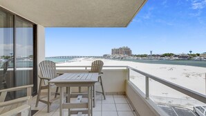 Un balcón con mesa y sillas, con vista a una playa y un puerto deportivo.