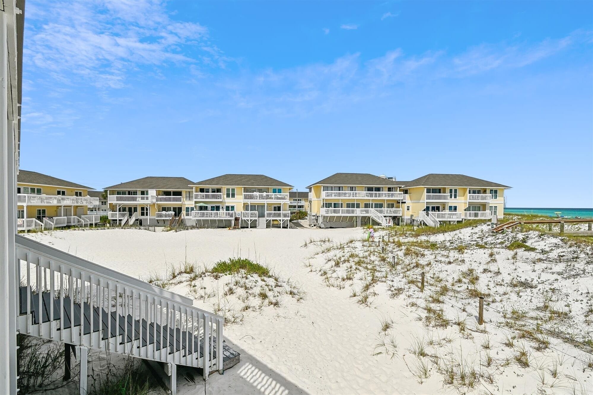 Un hôtel en bord de mer doté de nombreux balcons, une plage de sable en contrebas et un ciel bleu azur.