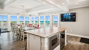 A spacious kitchen with a large island, a dining area with chairs, and a view of the beach.