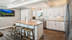 A modern kitchen with white cabinetry, a central island with stools, and a built-in oven.
