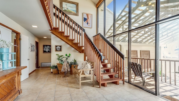 A spacious interior with a wooden staircase, large windows, and a balcony with outdoor seating. - The Other Castle 5 Bedroom Home by RedAwning (Destin)