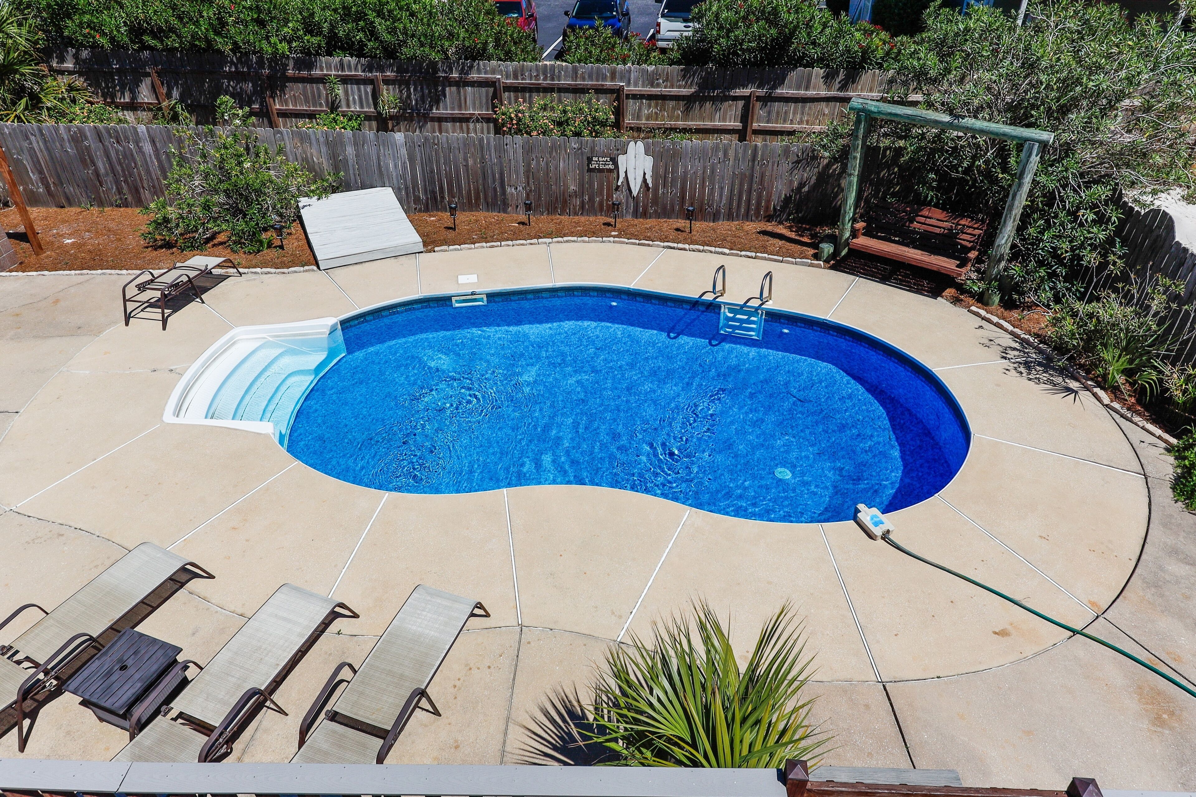 A backyard with a swimming pool, lounge chairs, and a wooden fence.