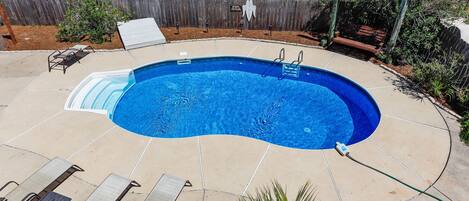 A backyard with a swimming pool, lounge chairs, and a wooden fence.
