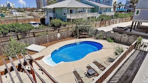 A swimming pool with a wooden deck and lounge chairs, surrounded by a wooden fence and vegetation. - The Other Castle 5 Bedroom Home by RedAwning (Destin)