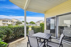 A covered patio with a table and chairs, a sliding glass door, and a view of residential buildings. - Sandpiper Cove 9125 2 Bedroom Condo by RedAwning (Destin)