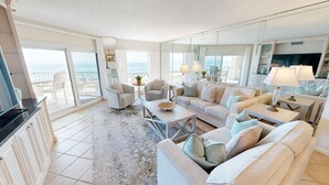 A spacious living room with a large sofa, a coffee table, and a view of the ocean through large windows. - Inlet Reef 205 2 Bedroom Apts by RedAwning (Destin)