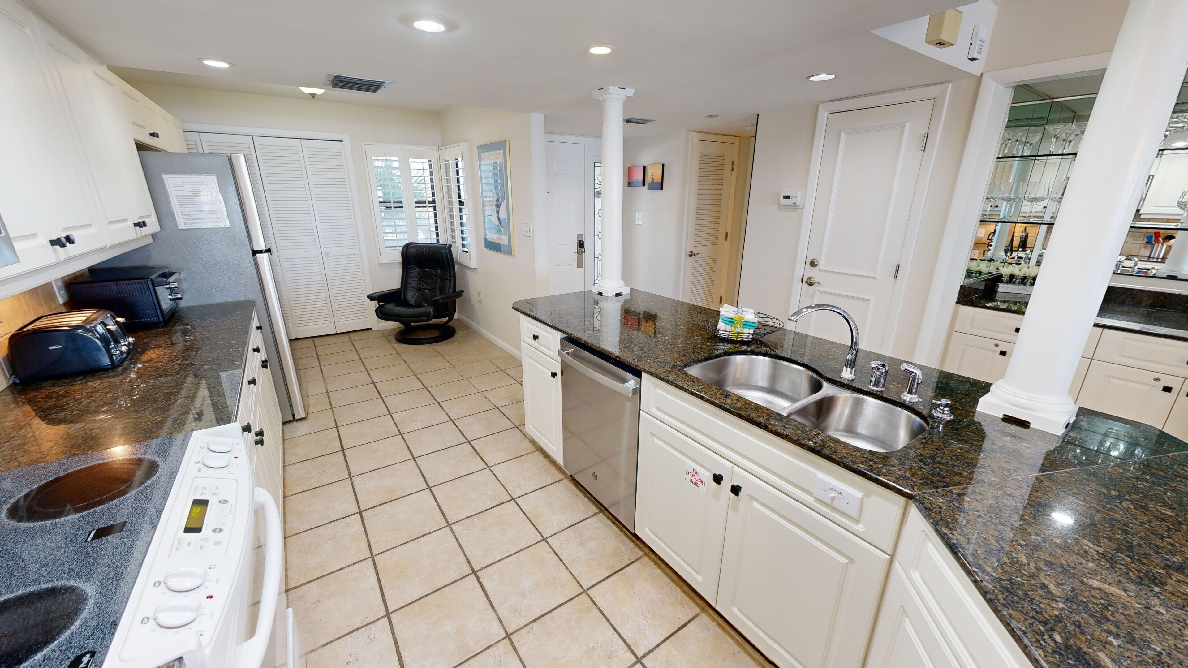 A modern kitchen with white cabinets, a granite countertop, a stainless steel sink, and a built-in dishwasher.