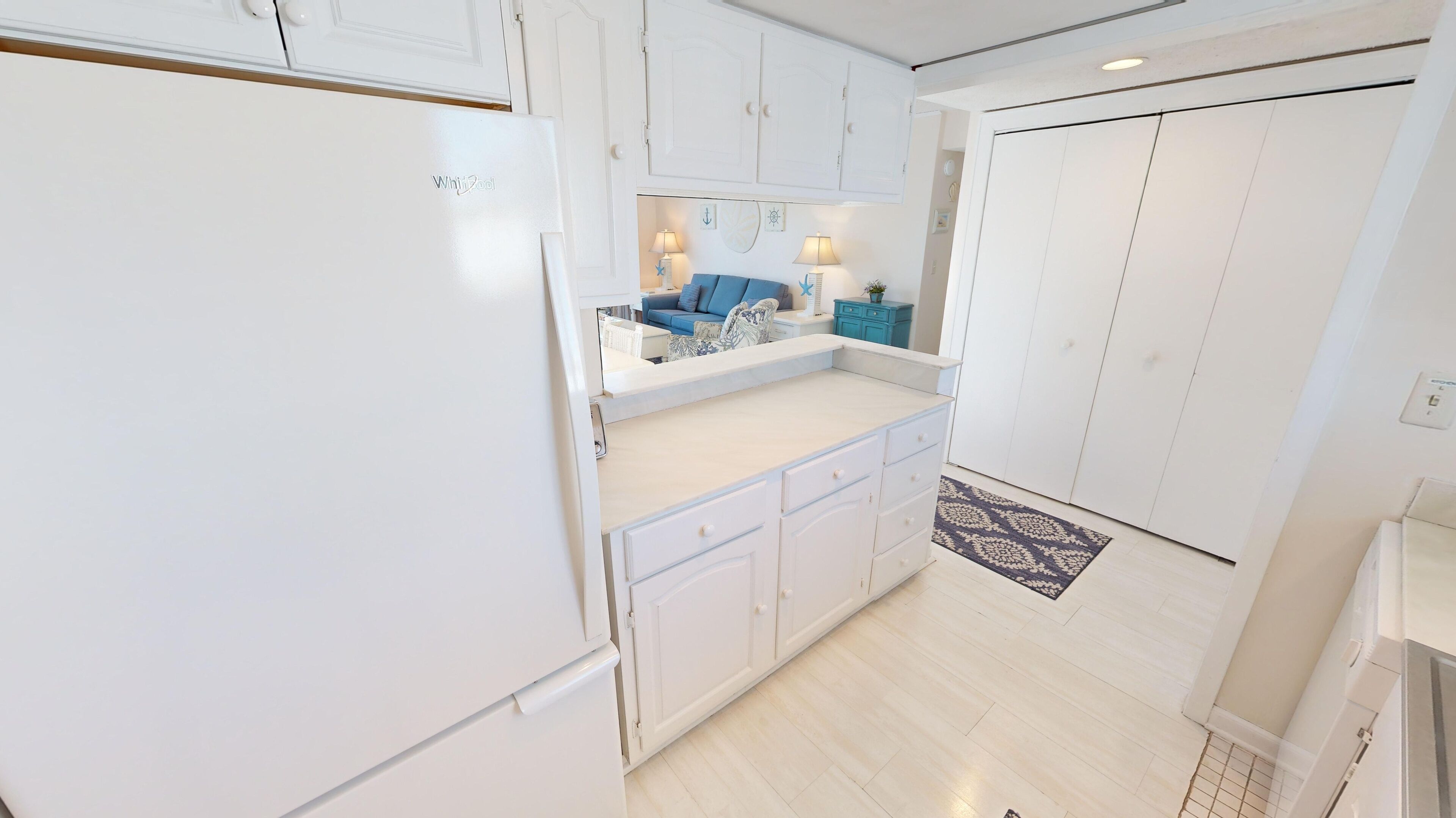 A kitchen with white cabinets, a white refrigerator, a blue sofa, and a patterned rug.