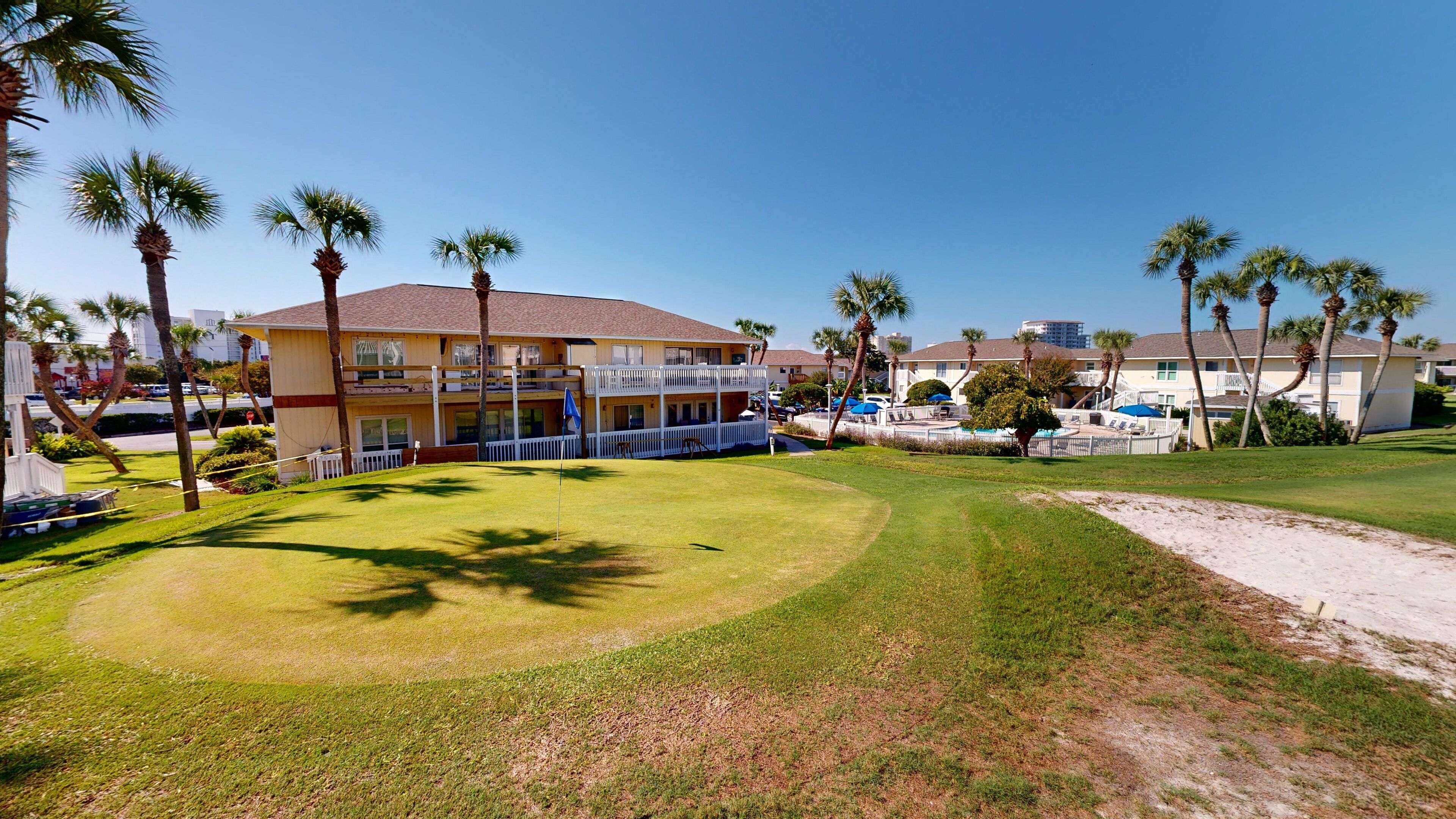 Ein Hotel mit Pool, Palmen und einem gepflegten Rasen.
