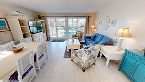 A well-lit living room with a dining area, a sofa, a TV, and a view through the glass door. - Sandpiper Cove 1082 2 Bedroom Condo by RedAwning (Destin)