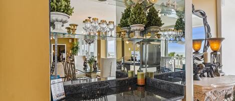 A modern kitchen with a granite countertop, a glass backsplash, and a large mirror reflecting the room.