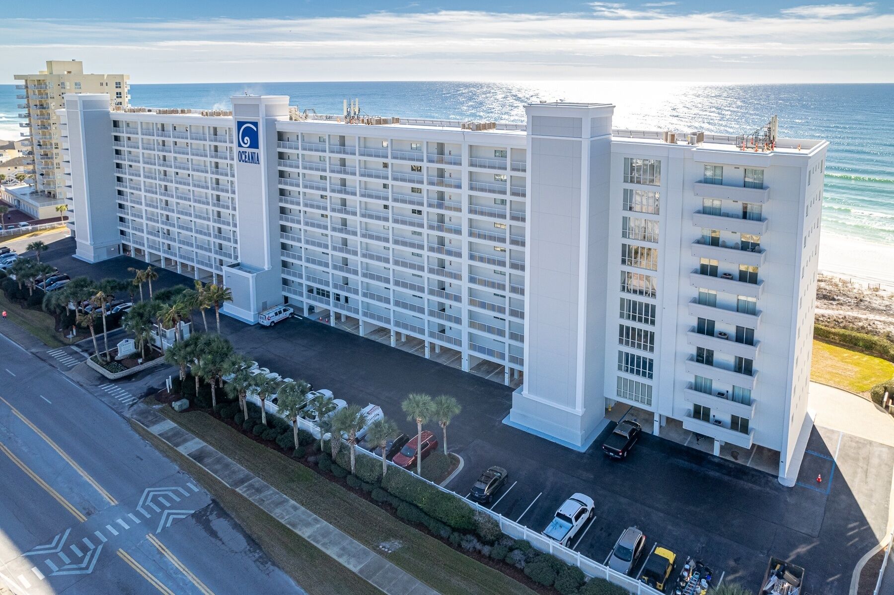 Un hôtel à plusieurs étages doté d’une cour intérieure, entouré d’un parking et offrant une vue sur la plage.
