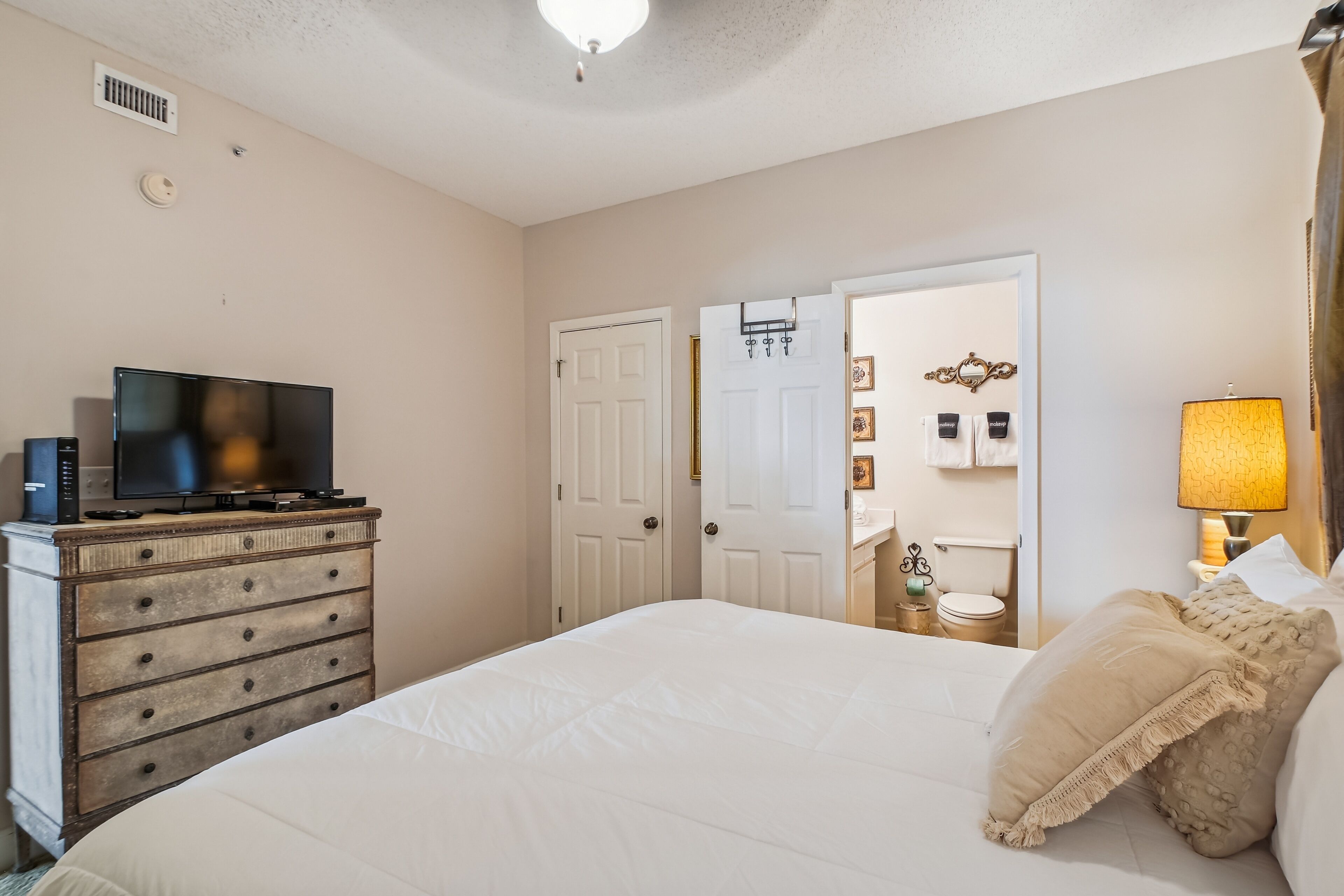A bedroom with a bed, dresser, television, and a door leading to a bathroom.