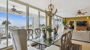 Uma sala de estar espaçosa com uma mesa de vidro e cadeiras, um lustre e vista para o mar.