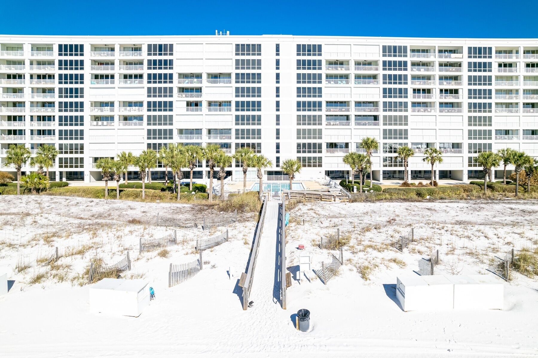 Ein modernes Hotel mit mehreren Etagen, einem Poolbereich und einem Sandstrand davor.