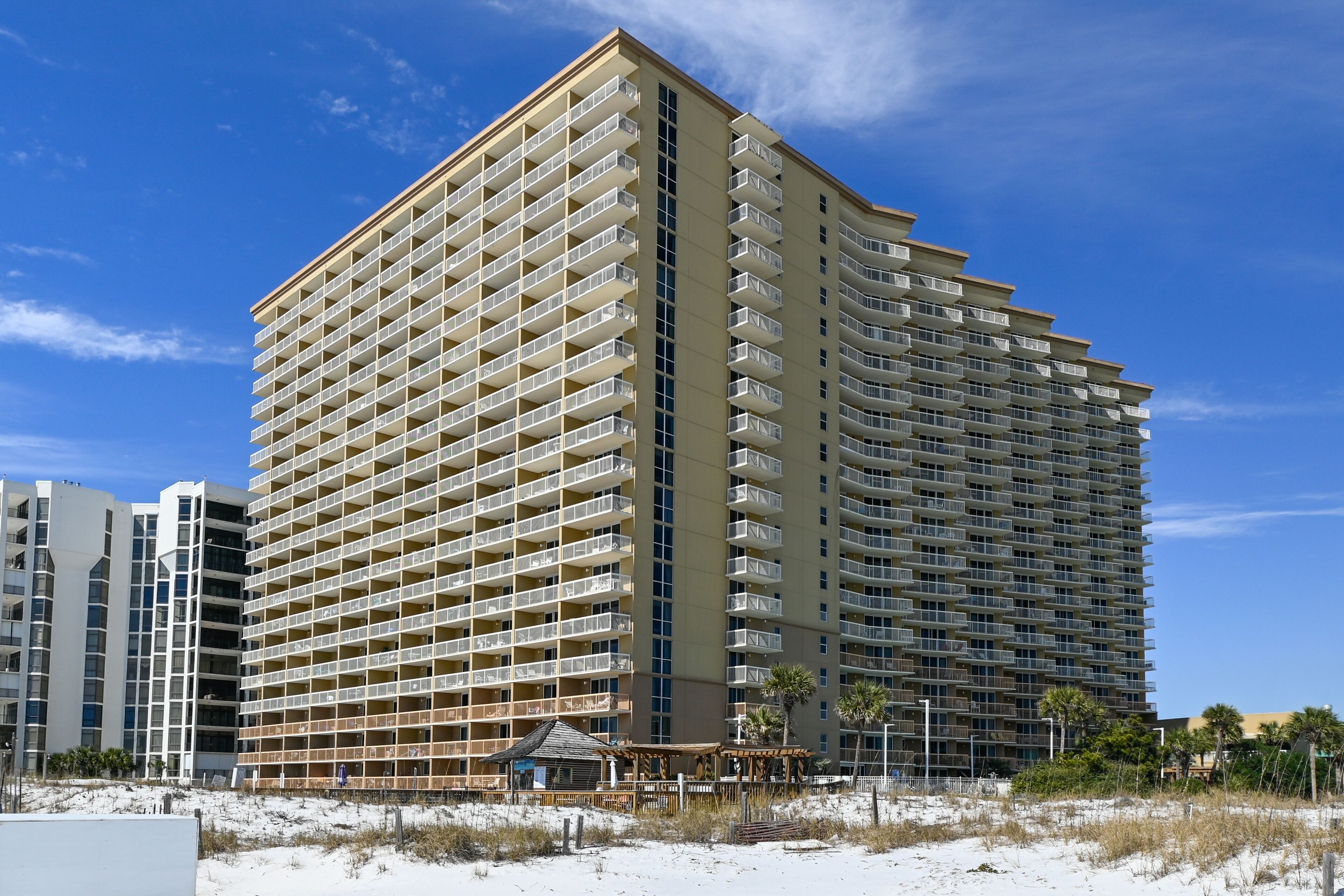 A high-rise hotel with multiple balconies, located near a beach.