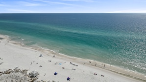 A beach with clear turquoise waters, sandy shore, and a few beach umbrellas. - Pelican Beach 1811 1 Bedroom Condo by RedAwning (Destin)