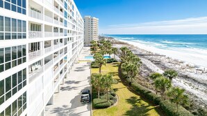 A modern hotel with a pool, a beach view, and a parking area.