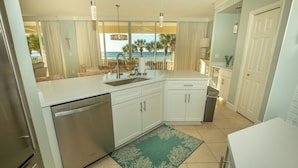 A kitchen with a dishwasher, white cabinets, a green rug, and a view of the beach.