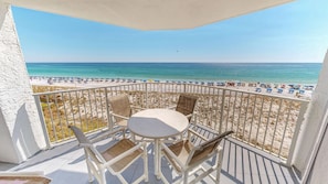 A balcony with a view of a beach, white railings, and a table with chairs.