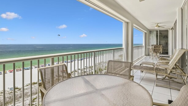 A balcony with a view of the ocean and beach, furnished with a table and chairs.