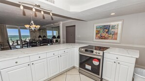 A modern kitchen with white cabinetry, a built-in oven, and a large window overlooking the ocean. - Shoreline Towers 1063 2 Bedroom Condo by RedAwning (Destin)