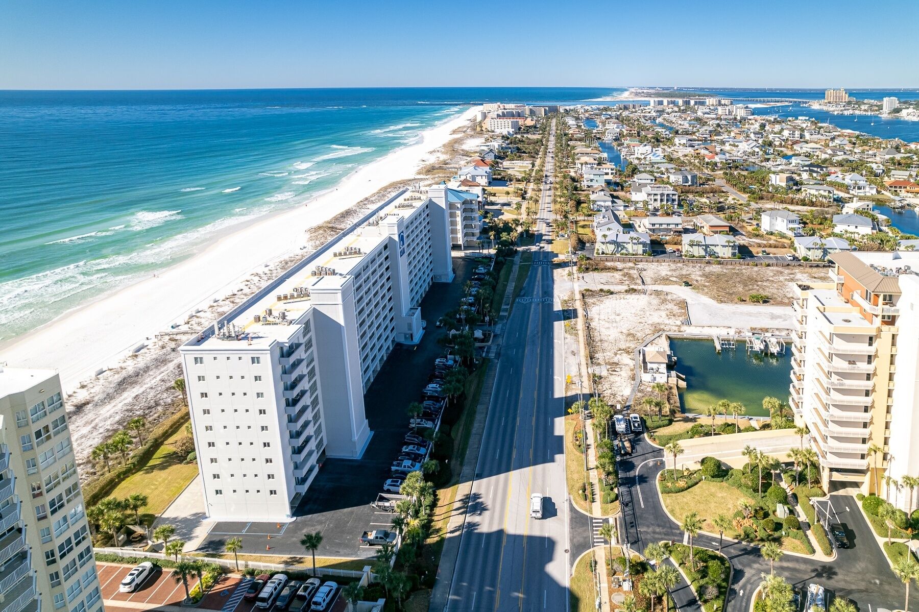 Un paisaje urbano costero con un hotel frente a la playa, un puerto deportivo y edificios residenciales densos.