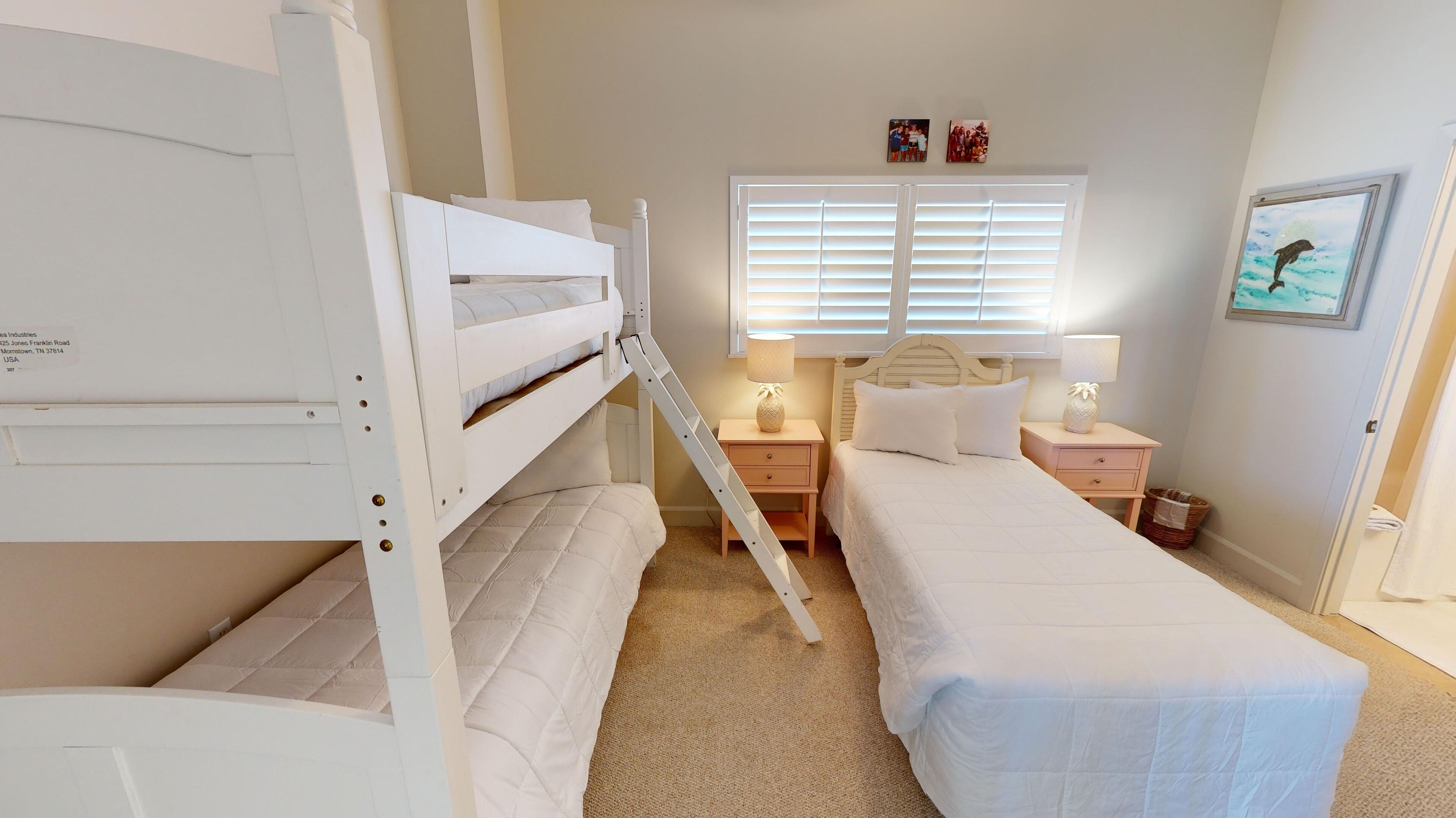 A bedroom with bunk beds, a bedside table with a lamp, a window with blinds, and a framed picture on the wall.