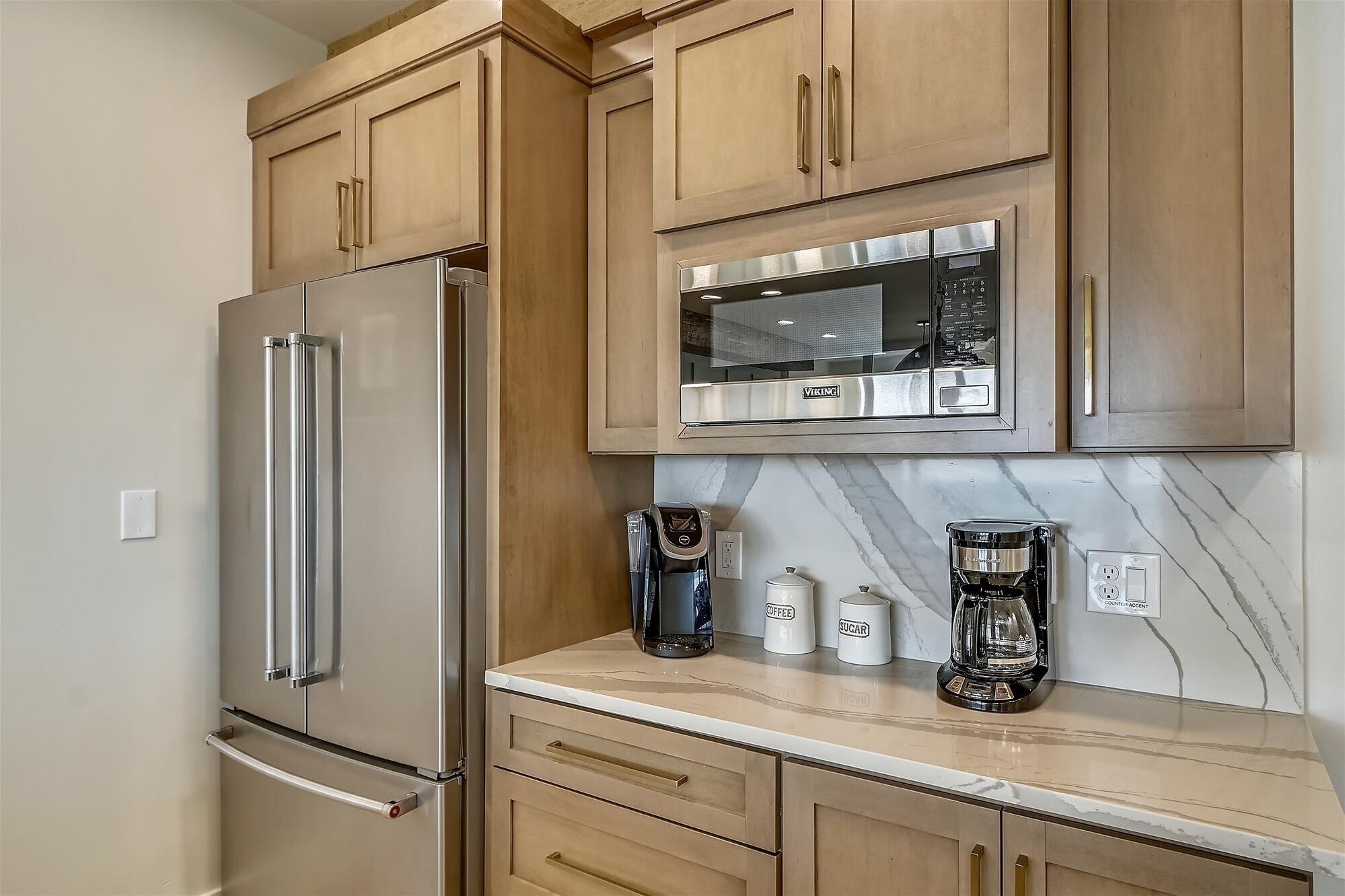 A kitchen with wooden cabinets, a stainless steel refrigerator, a microwave, and two coffee makers on the counter.