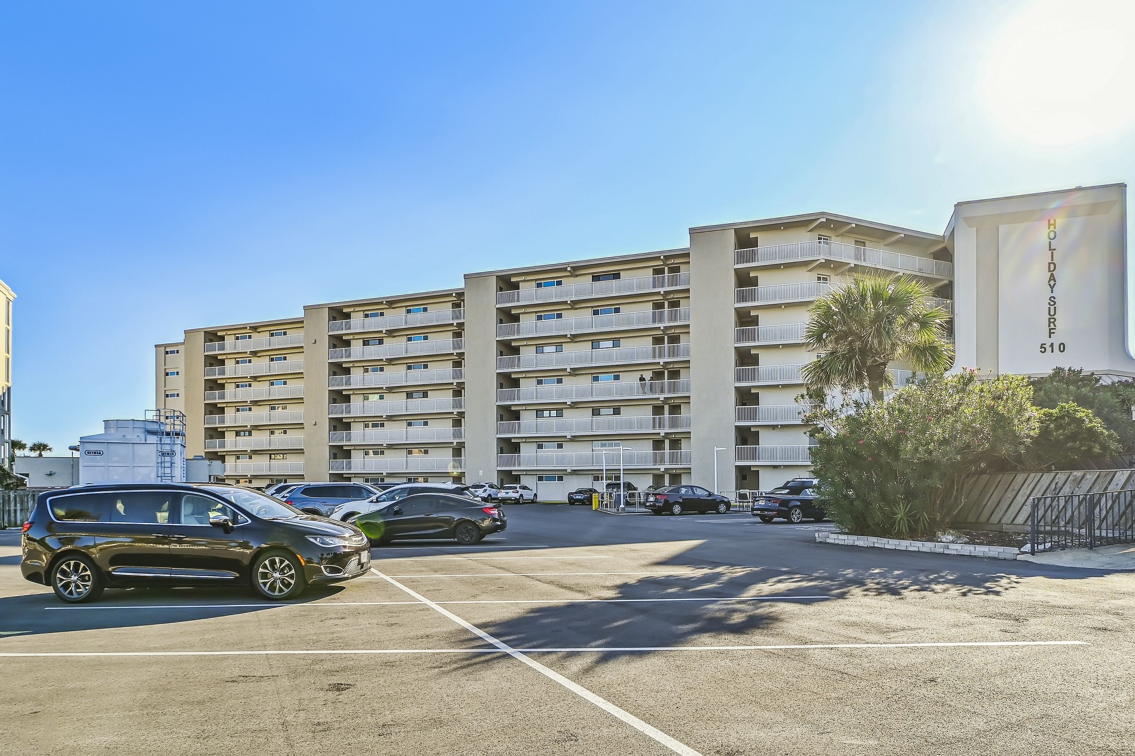 A multi-story hotel with balconies, a parking lot, and a sign reading "Holiday Surf 510".