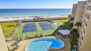A pool area with a tennis court, a swimming pool, and a beach view.