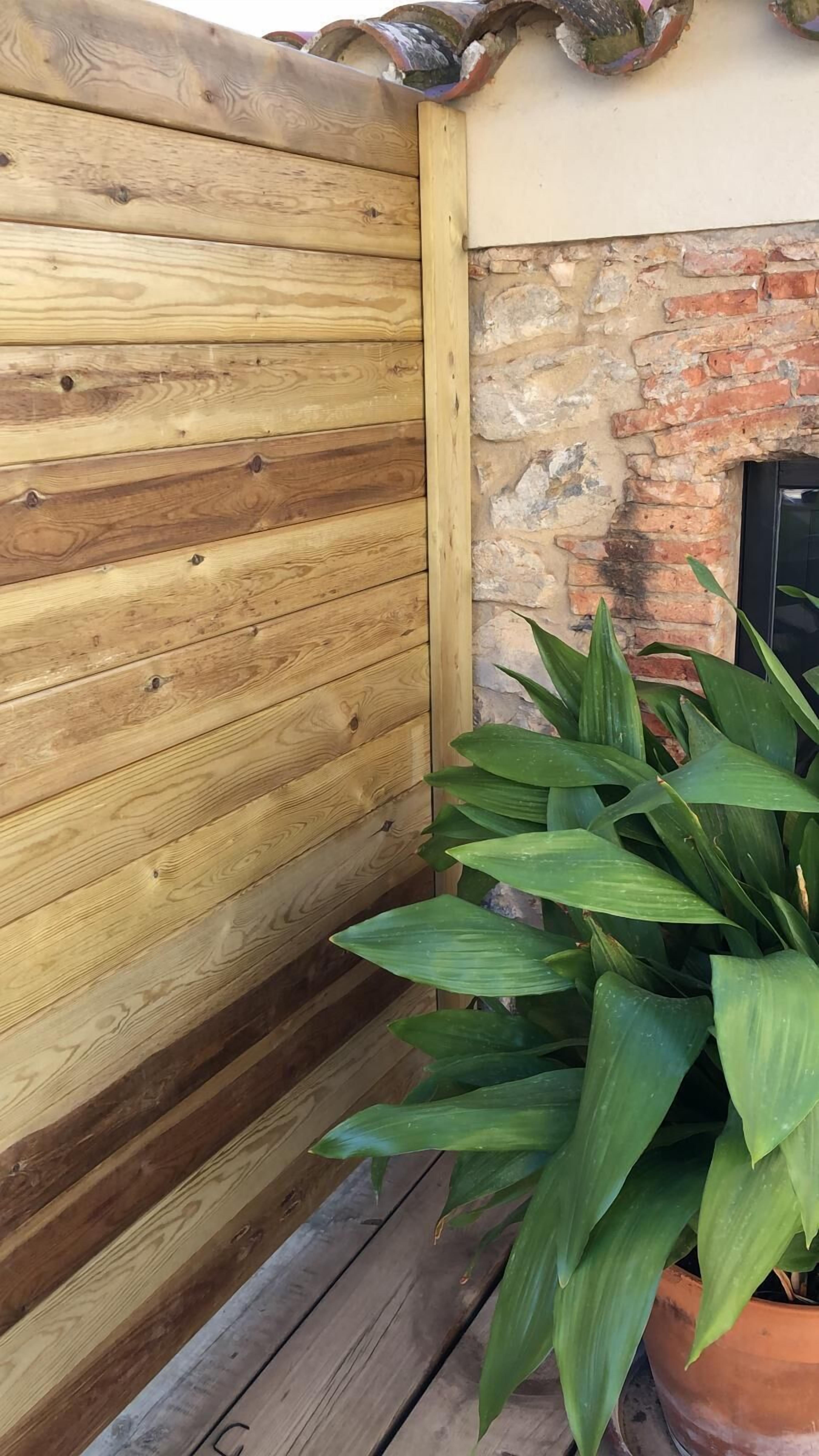 Une clôture en bois, un mur en briques et un pot de fleurs.