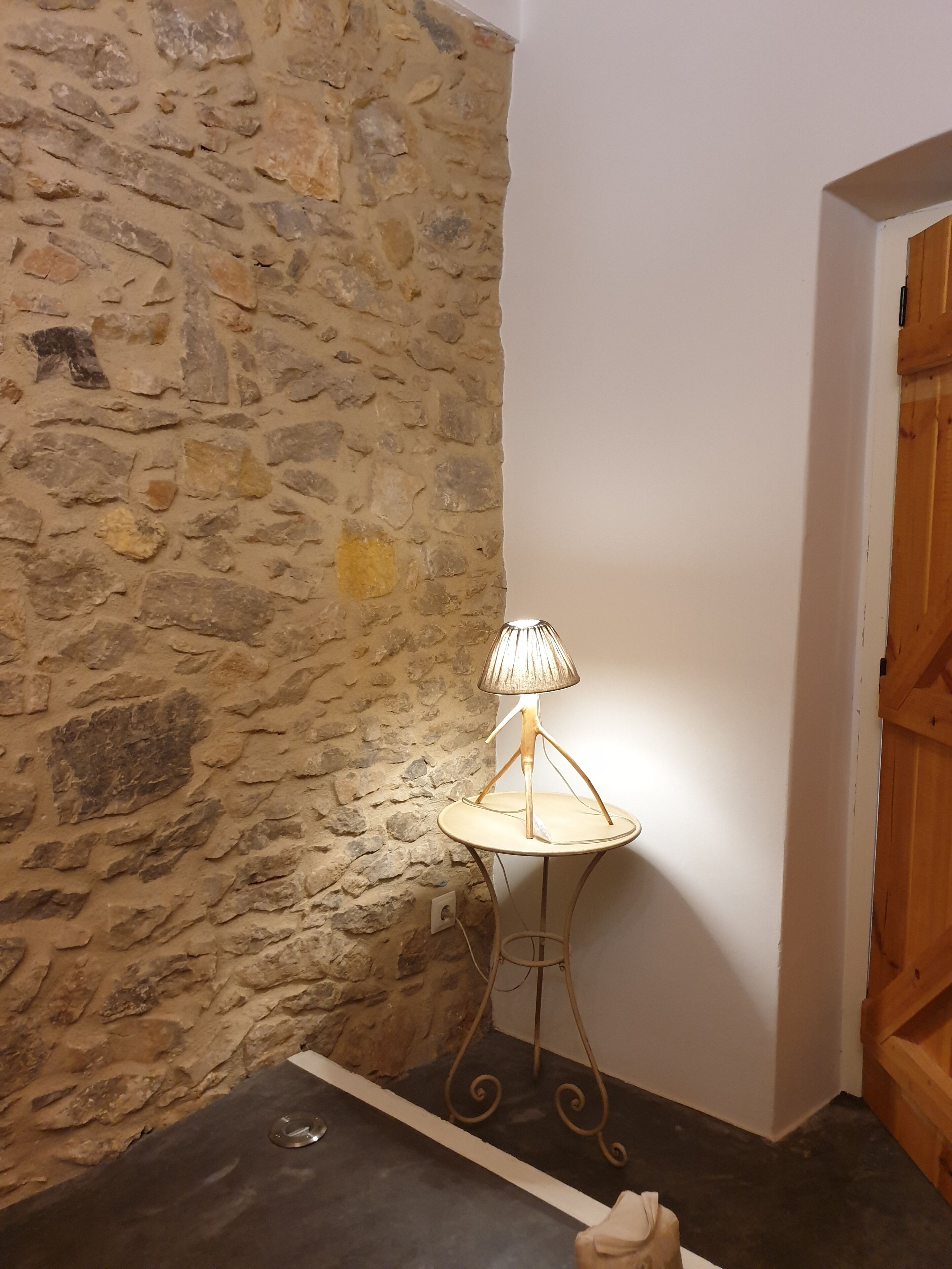 A corner with a stone wall, a small round table with a lamp, and a wooden door.