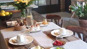 Une table à manger dressée avec des assiettes, des tasses et des bols de fruits, entourée de chaises et agrémentée d’un vase de fleurs.