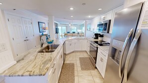 A modern kitchen with white cabinetry, a stainless steel refrigerator, and a marble countertop. - Inlet Reef 204 2 Bedroom Condo by RedAwning (Destin)