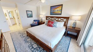 Un dormitorio con una cama grande, un cabecero de madera, dos mesitas de noche con lámparas, una silla y un cuadro en la pared.