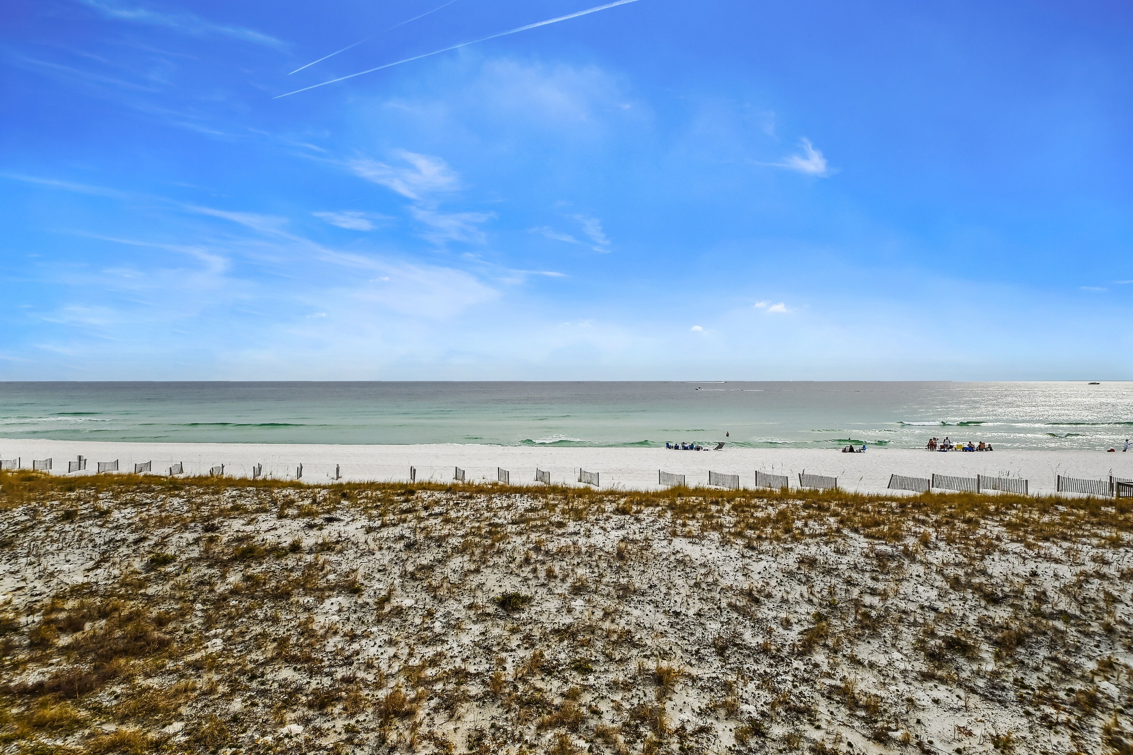 A beach with a sandy foreground and a wooden fence.