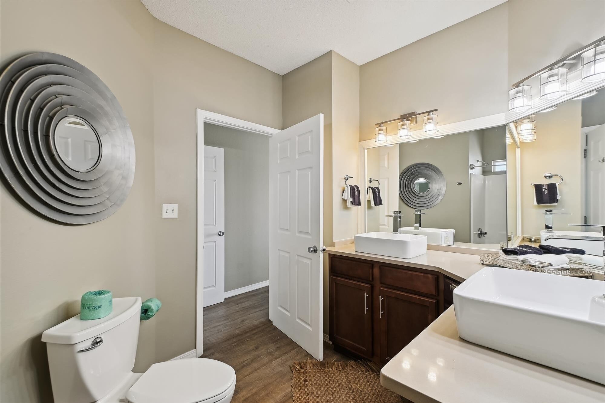A bathroom with a toilet, sink, and mirror. There is a door leading to another room.