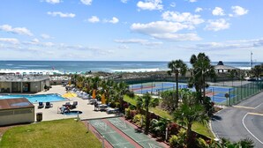 Un resort con piscina, canchas de tenis y vista a la playa.