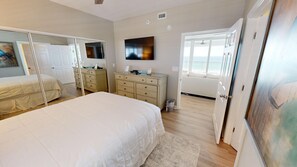 A bedroom with a large bed, a dresser, a TV, and a door leading to a balcony with a view.