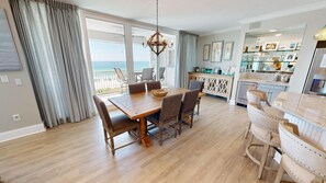 A dining area with a wooden table and chairs, a chandelier, and a view of the ocean.