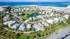 An aerial view of a coastal residential area with multiple buildings, a central green space, and a beach in the background. - Magnolia House 112 2 Bedroom Condo by RedAwning (Destin)